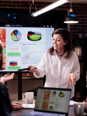 smiling-caucasian-woman-startup-office-doing-business-presentation-big-tv-screen-with-charts-front-team-confident-employee-presenting-growing-sales-statistics-late-night-meeting_482257-43087